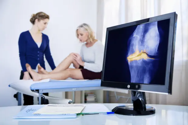 A screen showing a close-up of a person's bones on an x-ray and a person with knee pain in the background.