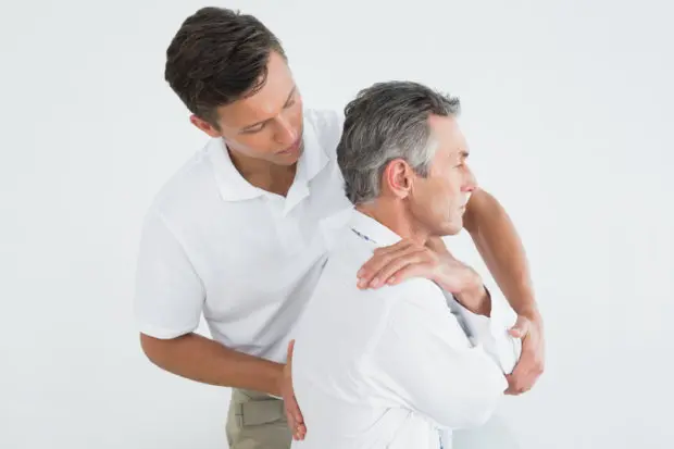 A man receiving a chiropractic adjustment from a chiropractor as he is sitting up.