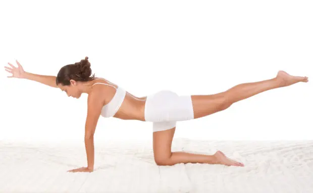 Woman that is doing a back workout to have a strong back, while she is in white workout clothes.