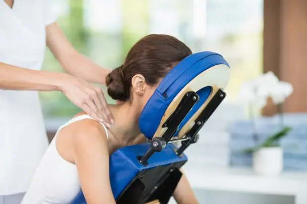 A woman who is in a massage chair in a chiropractic office getting a trigger point massage.