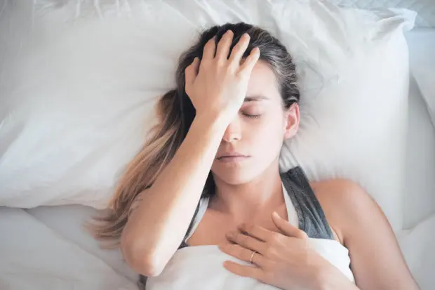 Woman who is still in bed clutching the front of her head due to migraine pain.