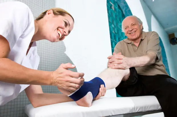 An elderly man that has a foot brace on his leg. It is being looked at by a medical professional at a chiropractic physical therapy center.