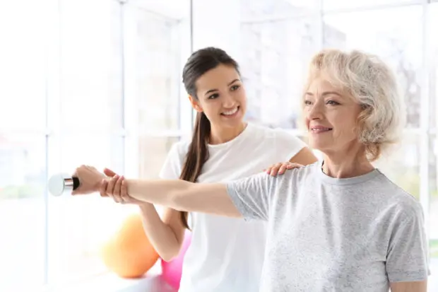 A beautiful elderly woman that is doing rehabilitative exercises with a trainer.