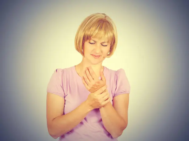 A blonde woman that is holding her hand and and frowning because of her neuropathy symptoms.