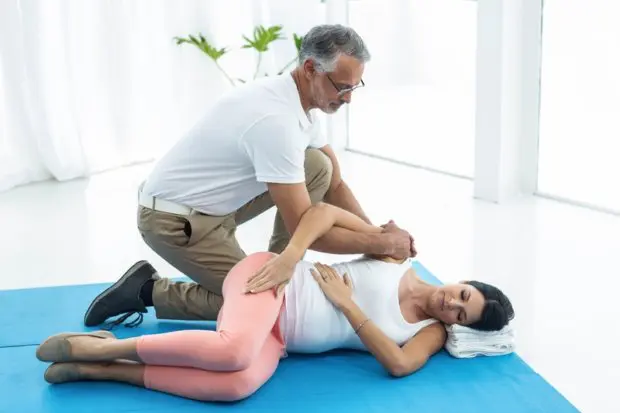 A chiropractor helping a pregnant woman with a few chiropractic adjustments on a floor mat.