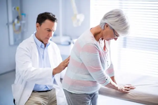 An elderly woman that is having her back looked at by a chiropractic professional for her back pain.