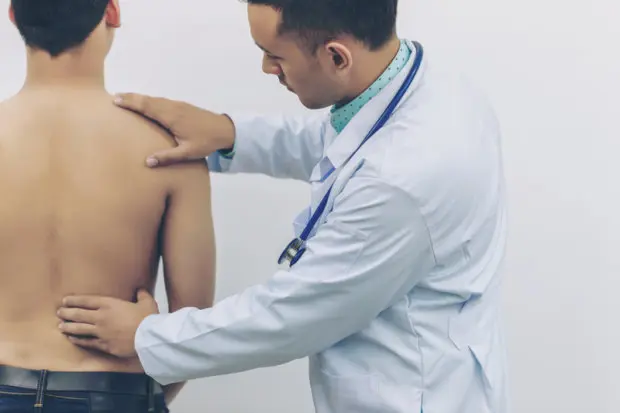 A medical professional is touching a patient's back to examine his back problems.