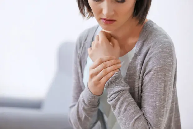 A woman that is looking down at the ground as she holds her painful wrist close to her.