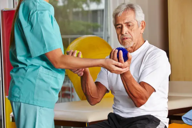 An elderly male that is doing rehabilitative therapy to help with his carpal tunnel syndrome.