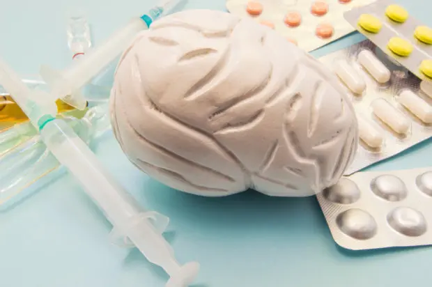 A model of a brain, which represents the nervous system, surrounded by syringes and medications.