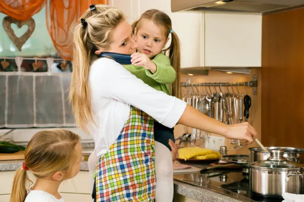 A busy, stressed out mom in a kitchen cooking, talking on the phone and holding a baby.